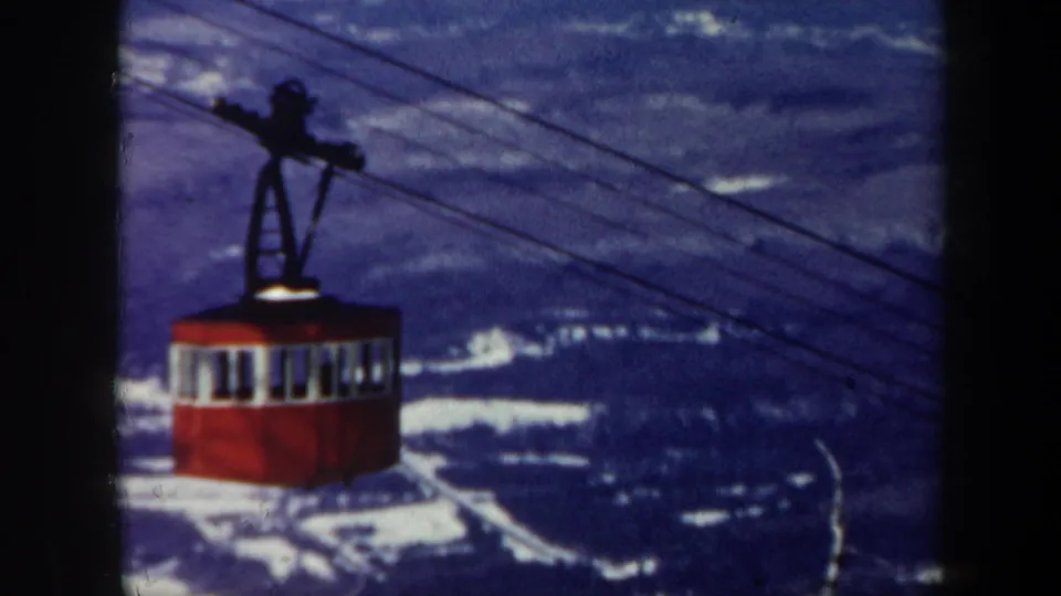 Red gondola lift cabin seen in 1962 Vermont home-movie footage, with cables crossing a blue mountain view.