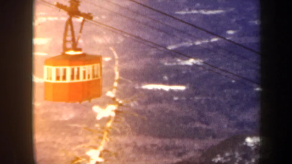 A red gondola cabin passes along its cables, with warm exposure flare and Vermont mountain slopes below.