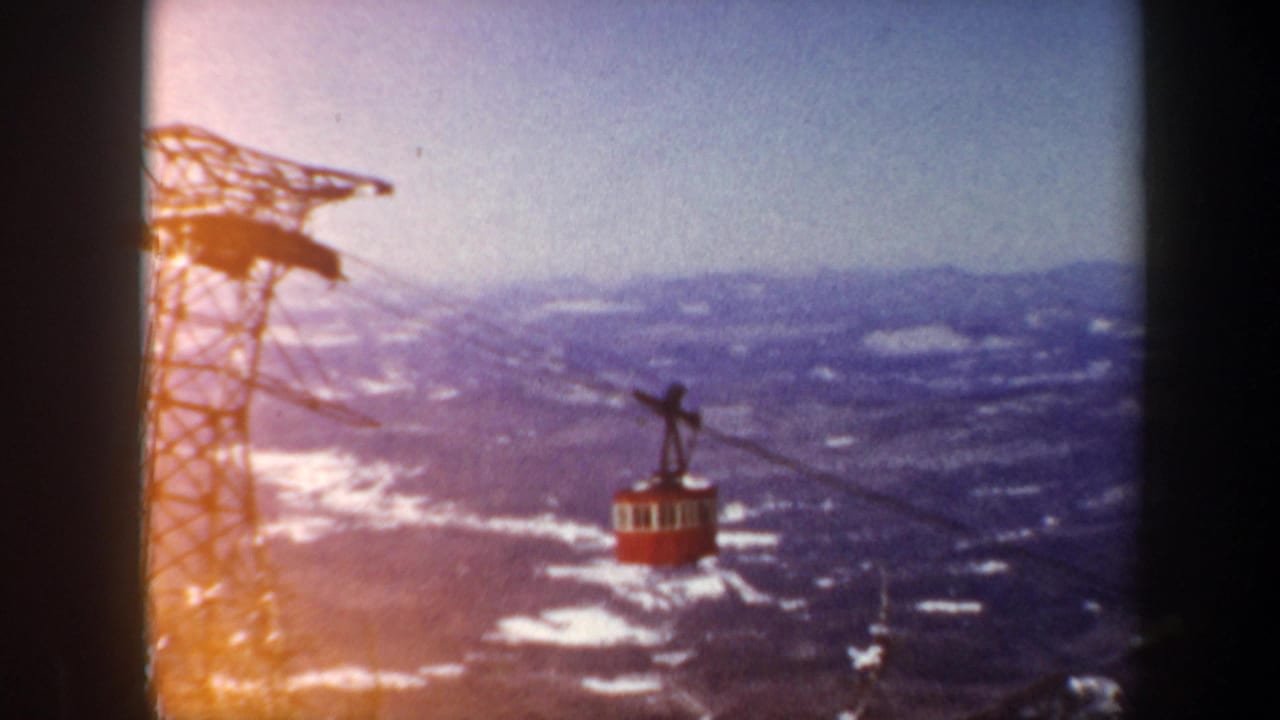 Red cable car suspended on wires beside a steel tower over snowy mountain terrain.