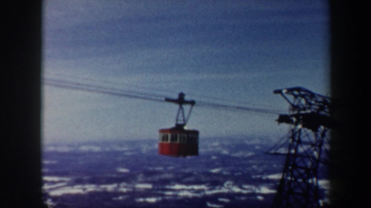 Red gondola lift car crosses overhead cables above a snow-covered Vermont mountain landscape in 1962 home-movie footage.