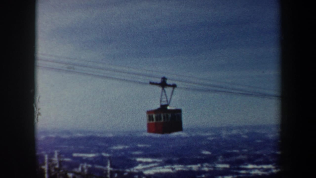 A red gondola car hangs from lift cables against distant snow-covered hills in Vermont, with the 8mm frame softened by grain and exposure variation.