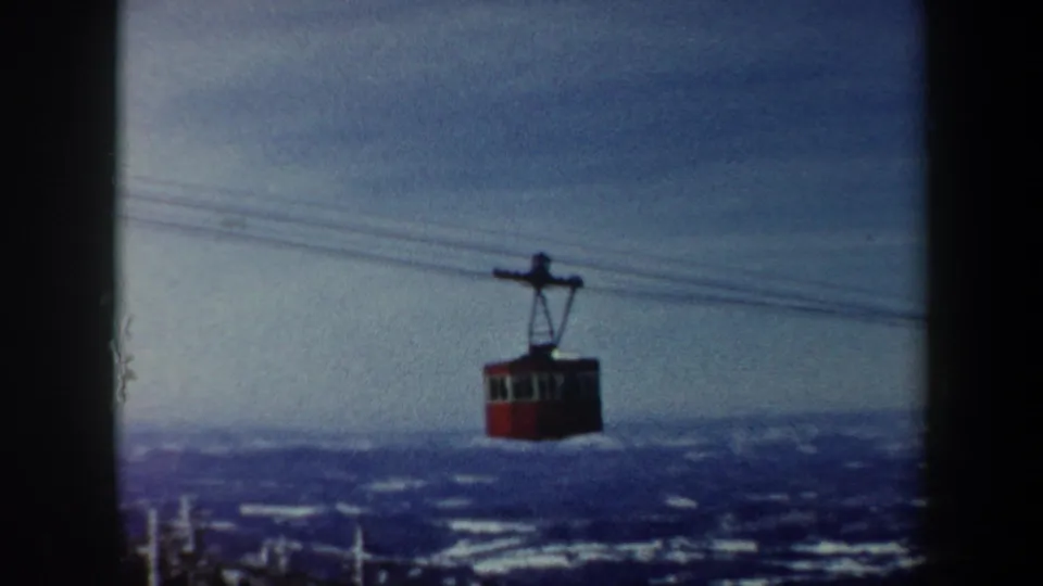 A red gondola car hangs from lift cables against distant snow-covered hills in Vermont, with the 8mm frame softened by grain and exposure variation.