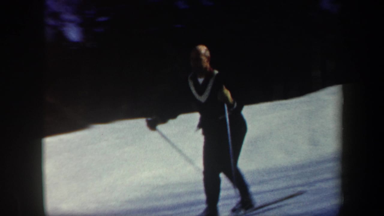 Adult skier in 1962 Vermont footage stands or moves on a sunlit snowy slope with dark evergreen trees in the background.