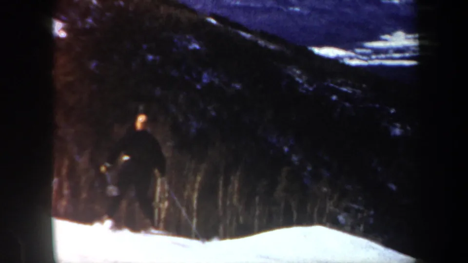 A skier appears lower in the frame near dark evergreens and bright snow in 1962 Vermont amateur ski footage.