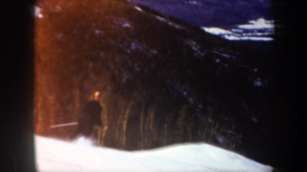 1962 Vermont 8mm frame showing a distant skier in dark clothing near a snowy slope and forested hillside.