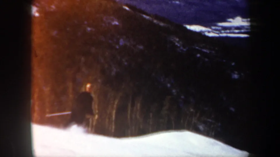 1962 Vermont 8mm frame showing a distant skier in dark clothing near a snowy slope and forested hillside.