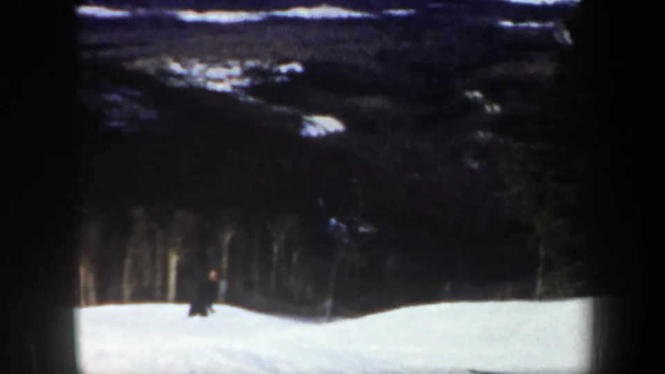 1962 Vermont 8mm frame with the skier farther downslope against dark trees and uneven winter light.