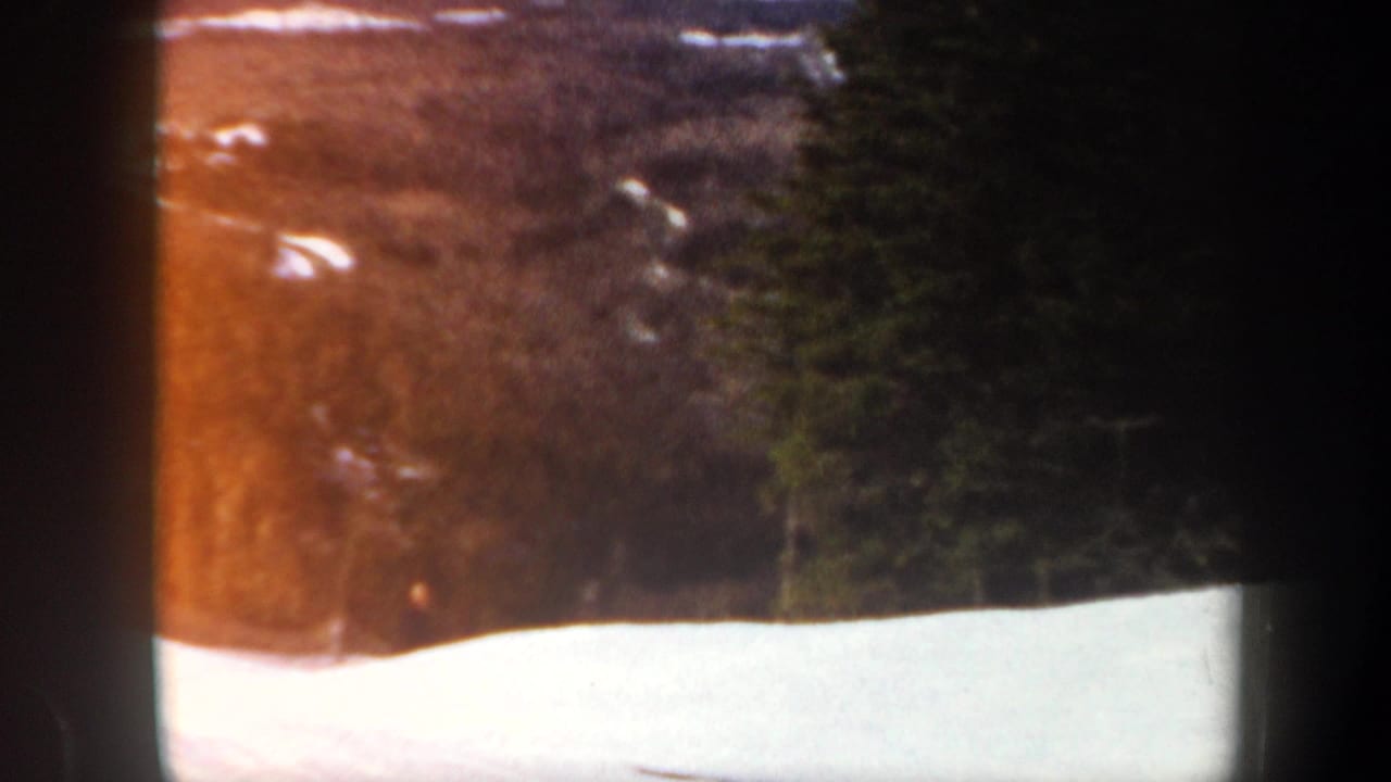 Snowy slope and evergreen trees seen through dark 8mm film borders.