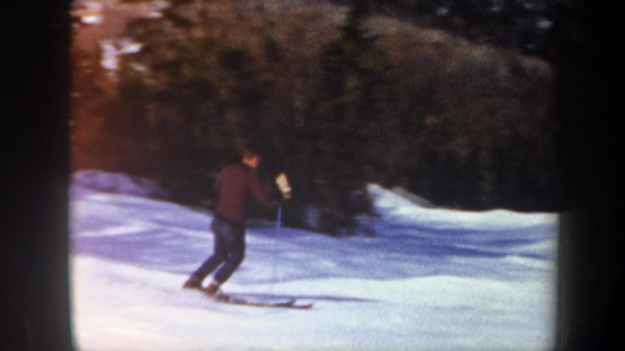A lone skier descends a Vermont snow slope in 1962 home-movie footage, with evergreen trees behind him.