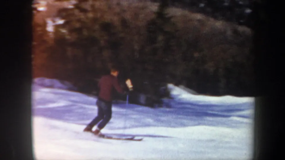A lone skier descends a Vermont snow slope in 1962 home-movie footage, with evergreen trees behind him.