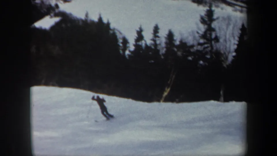 The skier appears small in the frame while moving across a snowy Vermont slope bordered by dark trees.