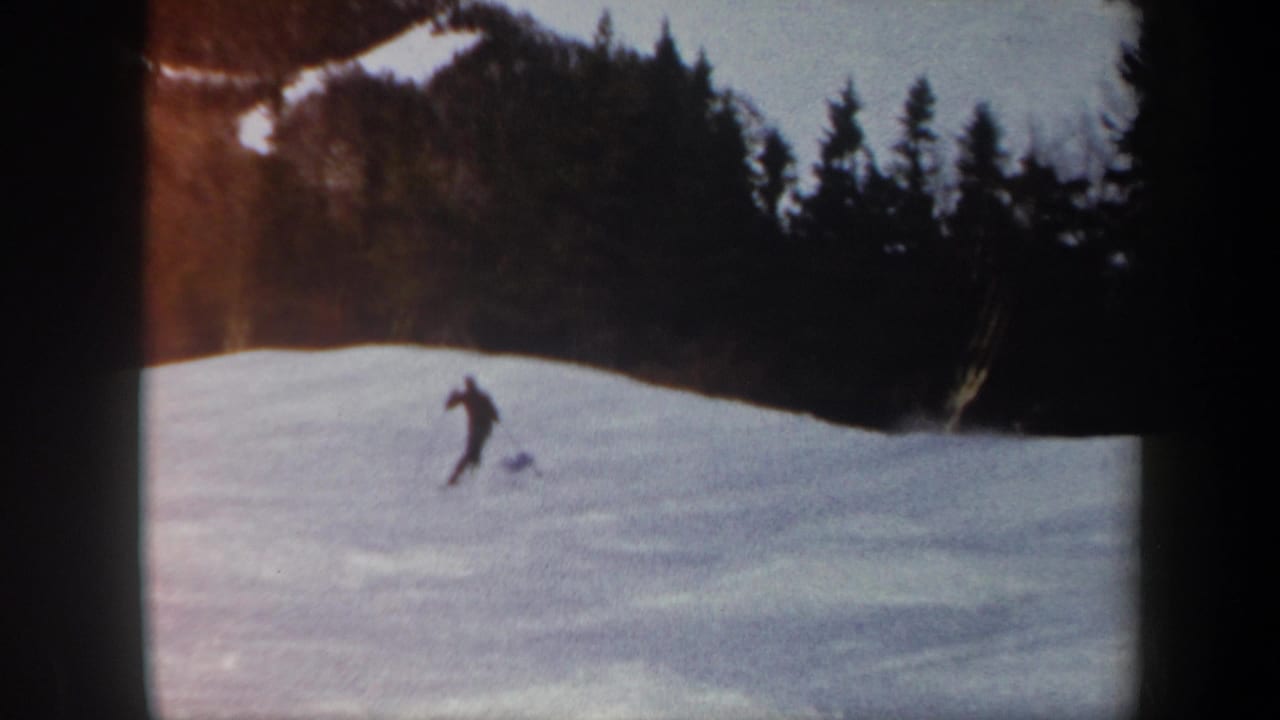 1962 Vermont 8mm frame showing a distant skier on a snow-covered slope with evergreens and patchy snow on the hillside behind.