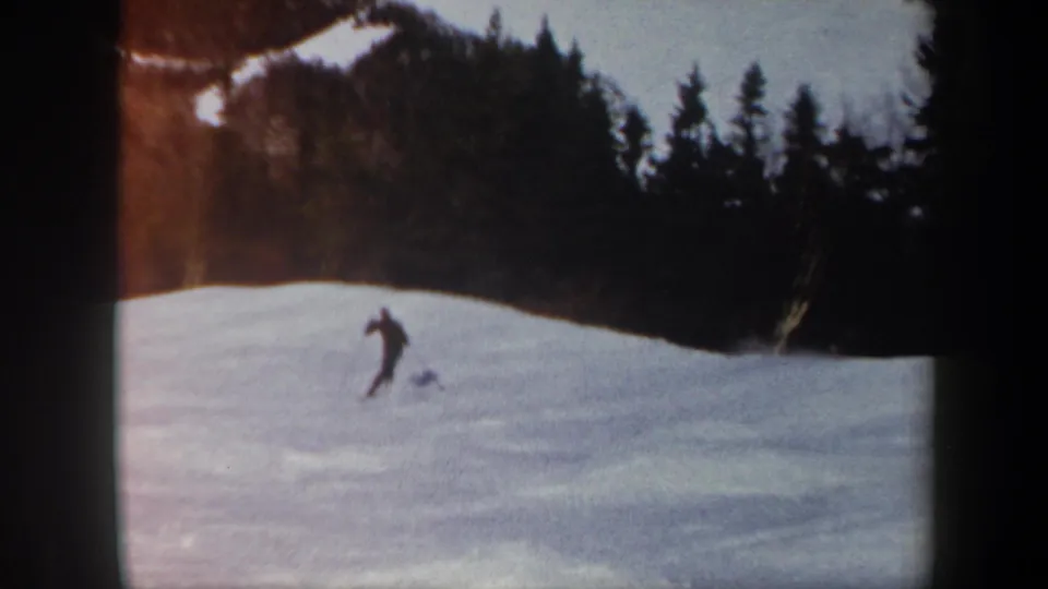 1962 Vermont 8mm frame showing a distant skier on a snow-covered slope with evergreens and patchy snow on the hillside behind.