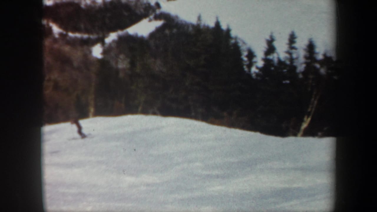 A lone skier appears small against a Vermont winter slope, with dark woods and exposed hillside snow in the background.