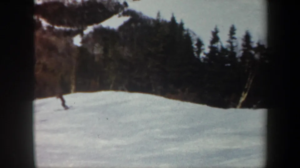 A lone skier appears small against a Vermont winter slope, with dark woods and exposed hillside snow in the background.