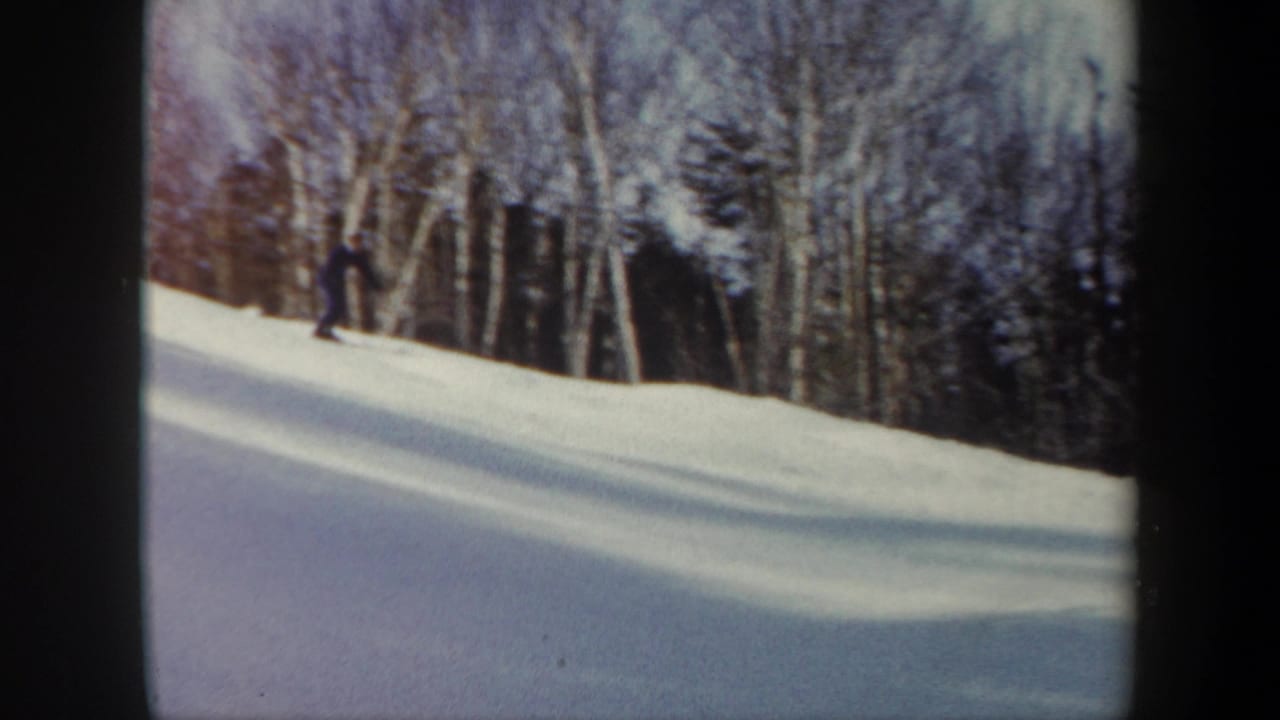 1962 Vermont 8mm frame showing a distant skier crossing a snowy forest slope bordered by bare birch trees and evergreens.