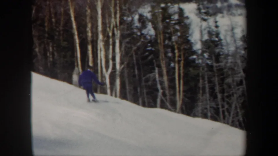 1962 Vermont 8mm frame showing the skier farther downhill against a dense stand of winter trees.