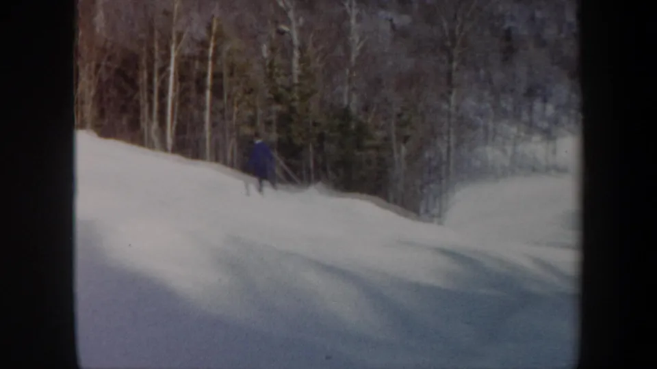 The skier is seen farther away near the wooded edge of the slope, with dark 8mm frame borders visible.