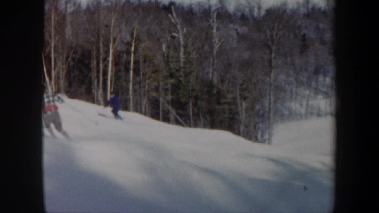 1962 Vermont 8mm frame showing skiers on a snowy downhill slope near a winter forest.