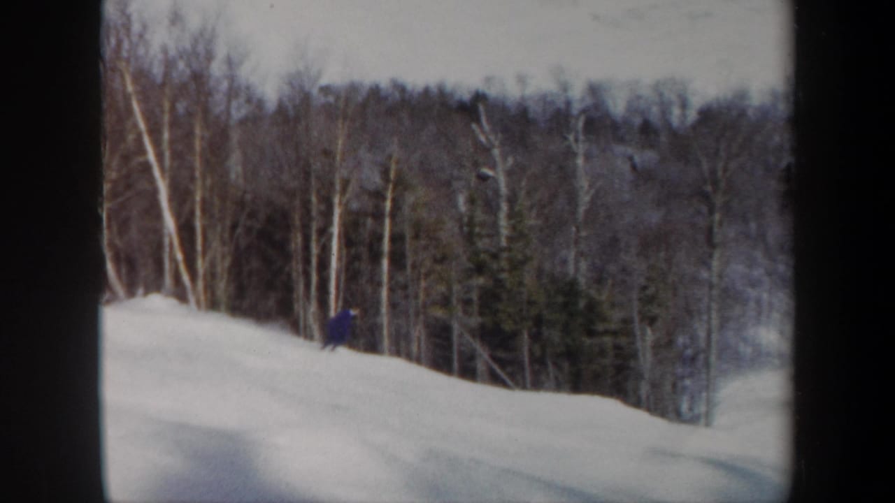 1962 Vermont home-movie frame with a skier crossing a snowy slope beside dense winter woods.