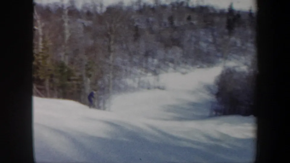 1962 Vermont 8mm frame showing a lone skier on a broad snow-covered hill with forested slopes beyond.
