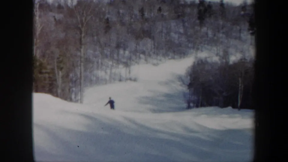 1962 Vermont home-movie frame of a skier moving downhill on a snowy run framed by winter forest.