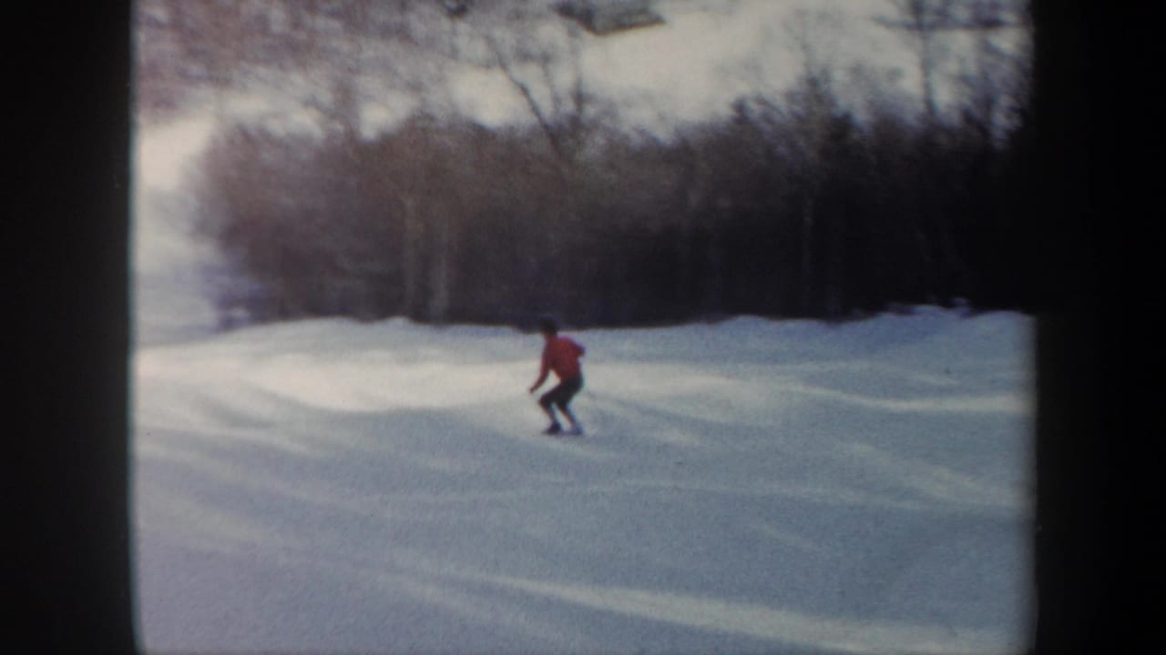 The skier continues downhill across a snowy Vermont slope, framed by winter trees and soft 8mm color.