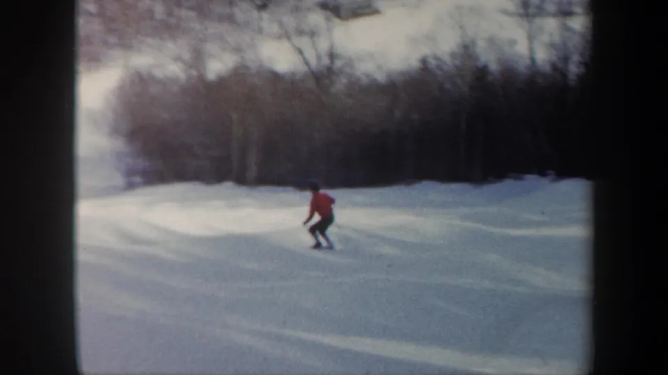 The skier continues downhill across a snowy Vermont slope, framed by winter trees and soft 8mm color.
