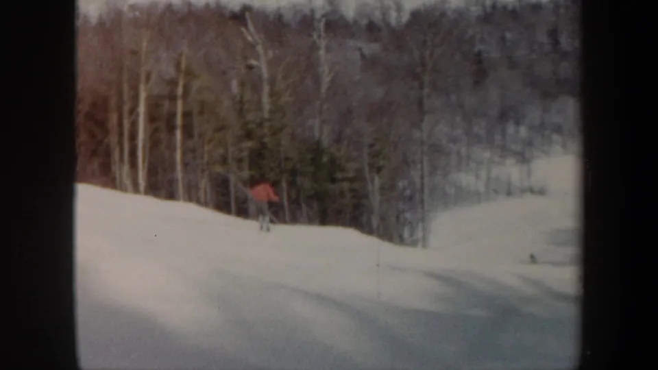 The skier passes near the wooded edge of the Vermont snow slope, recorded in grainy 8mm home-movie footage.
