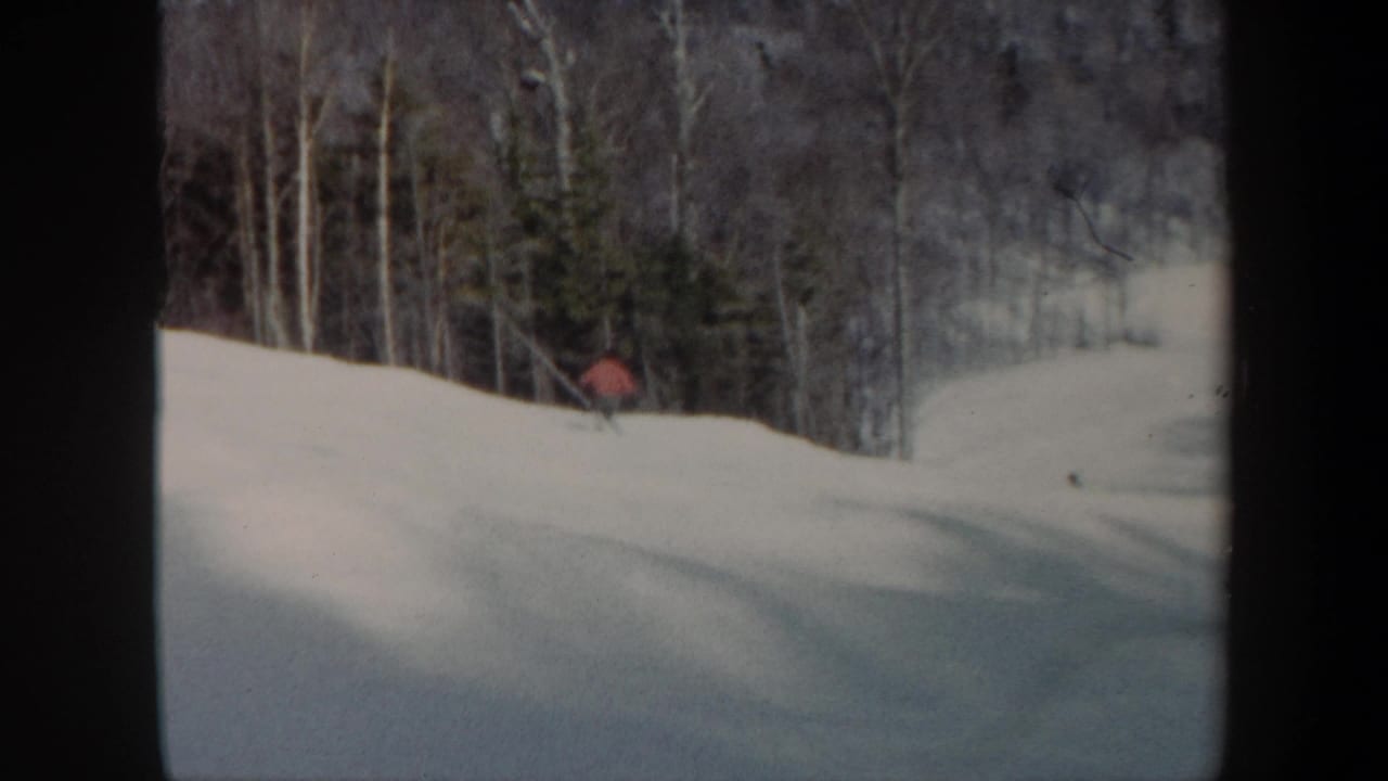 1962 Vermont 8mm frame showing a distant skier in red crossing a broad snow-covered ski slope with bare trees and evergreens behind.