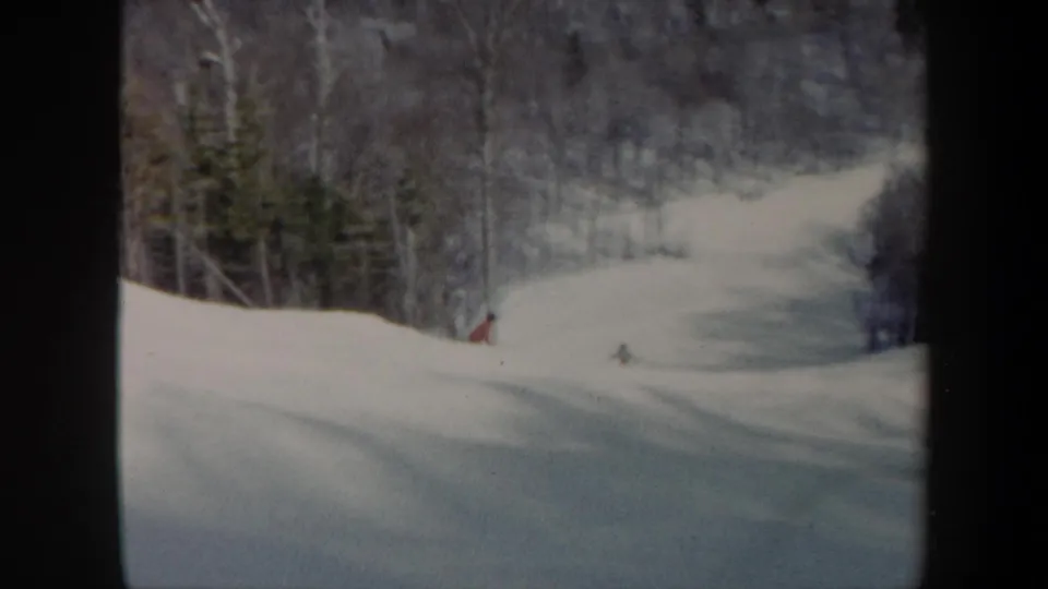 1962 Vermont ski slope seen in soft 8mm color, with distant skiers moving down open snow between wooded edges.