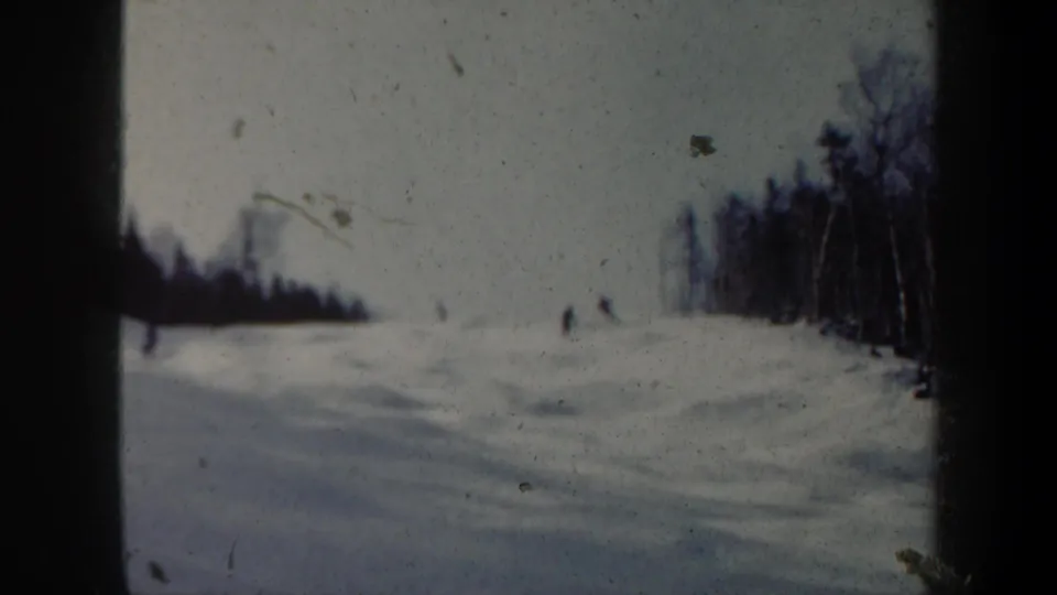 Faded 8mm frame from 1962 Vermont showing distant skiers on a snowy run with woods at the right edge and visible film dust.