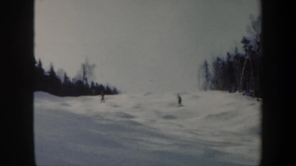 1962 Vermont home-movie frame showing skiers spaced across a snowy, uneven ski run with woods on both sides.