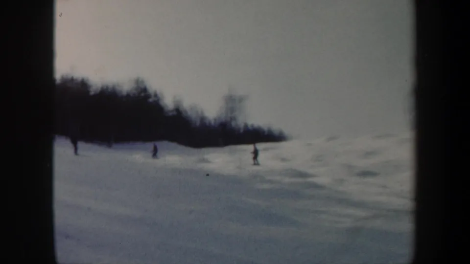 1962 Vermont 8mm frame with multiple skiers spread across a snowy mogul slope beneath a dark wooded ridge.
