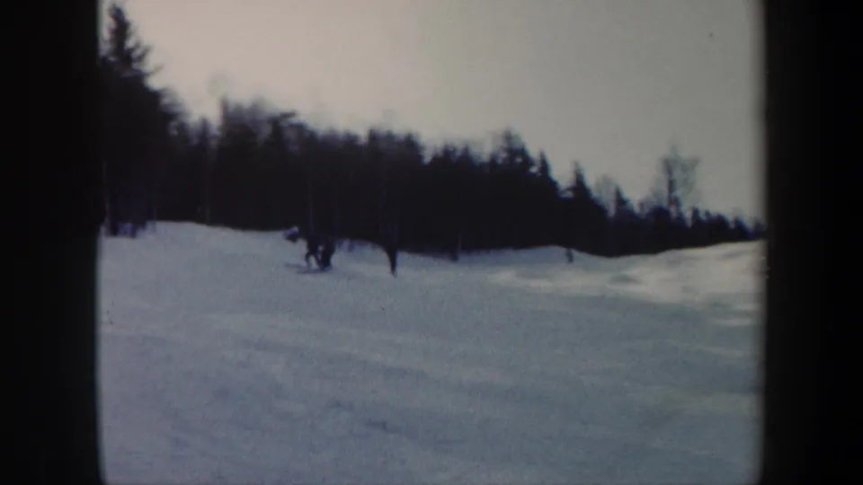 Skiers appear as small figures on a Vermont snow slope, with a dark wooded ridge behind them.