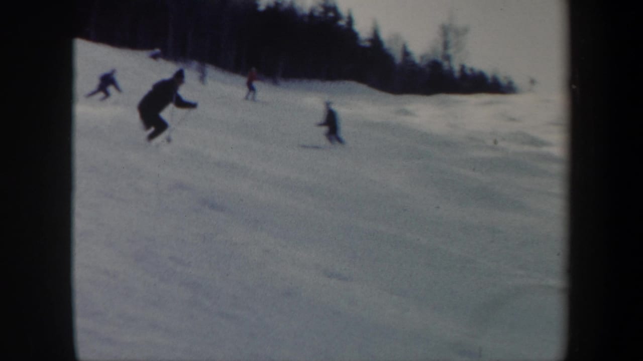 A skier moves downhill in the foreground while other skiers cross the snowy slope behind.