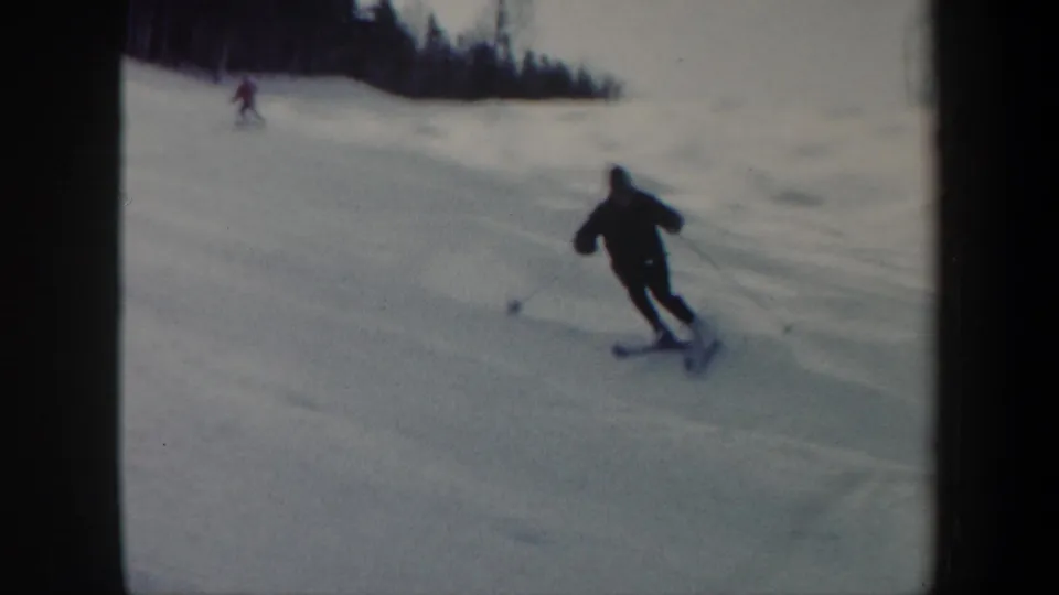 1962 Vermont 8mm frame showing a dark-clad skier turning downhill, with another skier faintly visible near the upper slope.