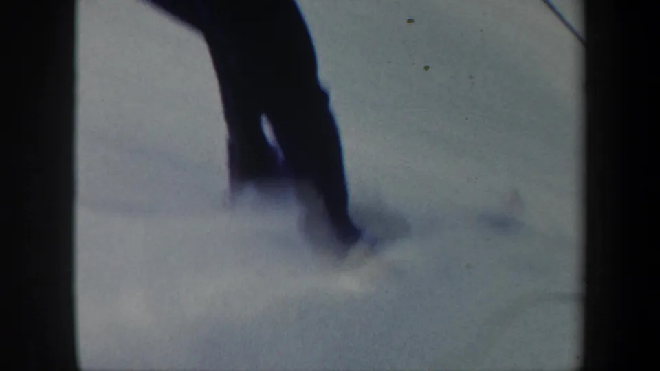 Soft 8mm frame from the Vermont skiing clip, showing a close blurred pass of a skier on snow.