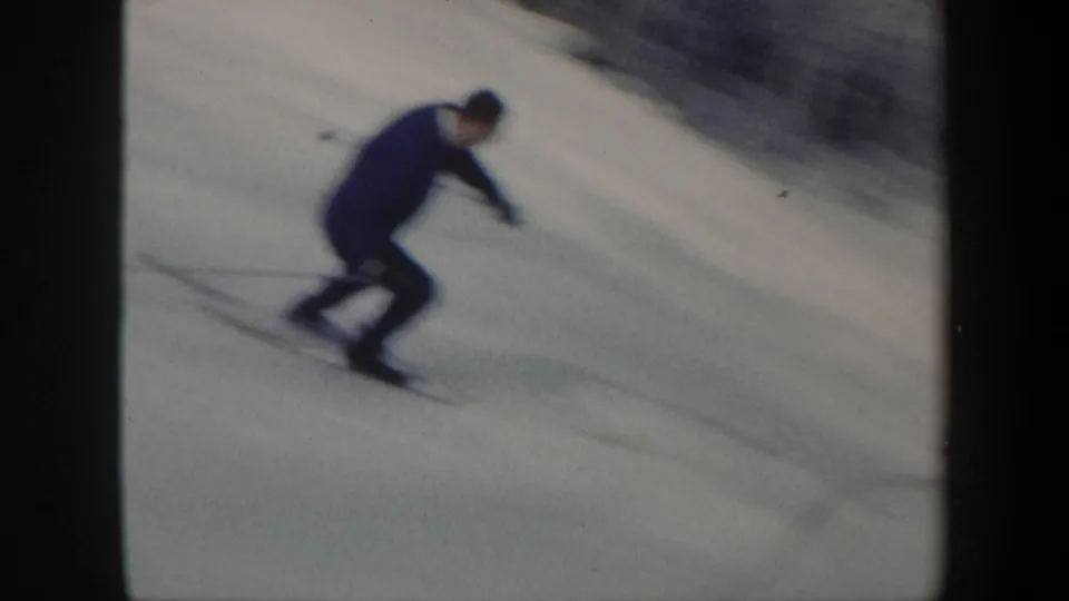 1962 Vermont 8mm frame showing an adult skier in a low crouch turning across a snowy slope.