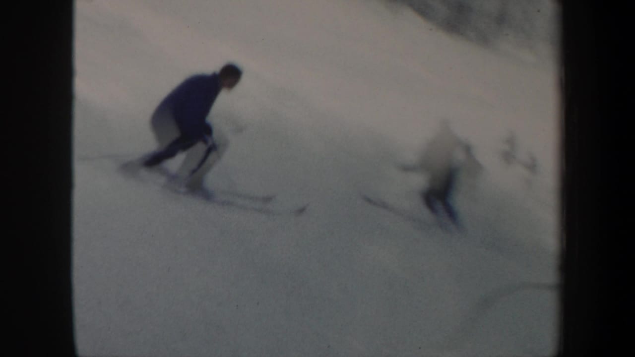 In 1962 Vermont home-movie footage, several skiers descend a snowy slope near a distant treeline.