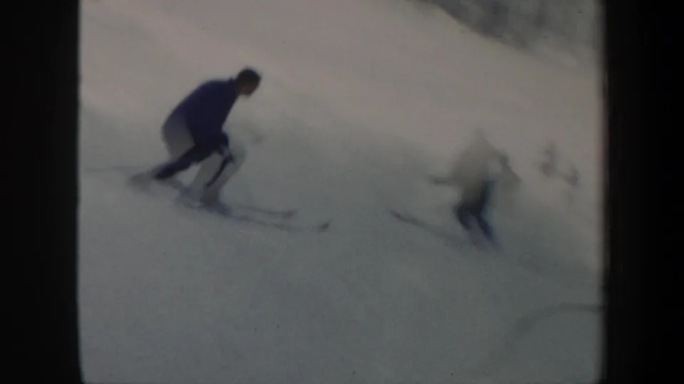 In 1962 Vermont home-movie footage, several skiers descend a snowy slope near a distant treeline.