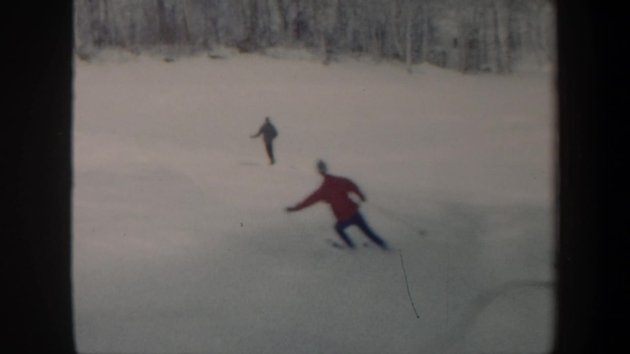 1962 Vermont home-movie frame showing distant skaters on a frozen lake, including one in a red jacket near the foreground.
