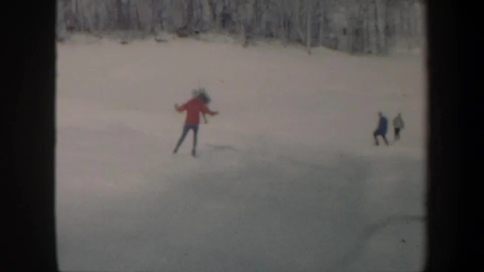 1962 Vermont frame with a red-jacketed skater on open ice and two darker figures near the edge of the snowy lake.