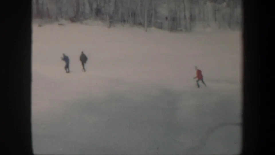 1962 Vermont frame showing widely spaced skaters on a snowy frozen lake, with a red-jacketed figure at the right.