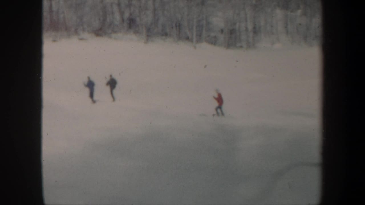 1962 Vermont home-movie frame showing three distant skiers descending an uncrowded snowy slope near bare trees.