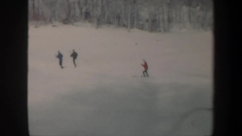 1962 Vermont home-movie frame showing three distant skiers descending an uncrowded snowy slope near bare trees.