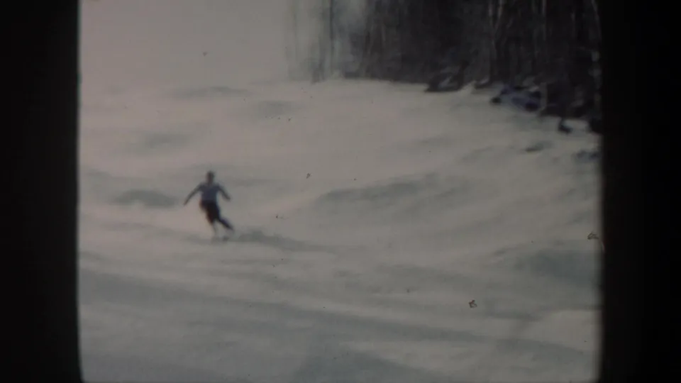 1962 Vermont 8mm frame of one skier turning through soft snow with leafless woods in the background.