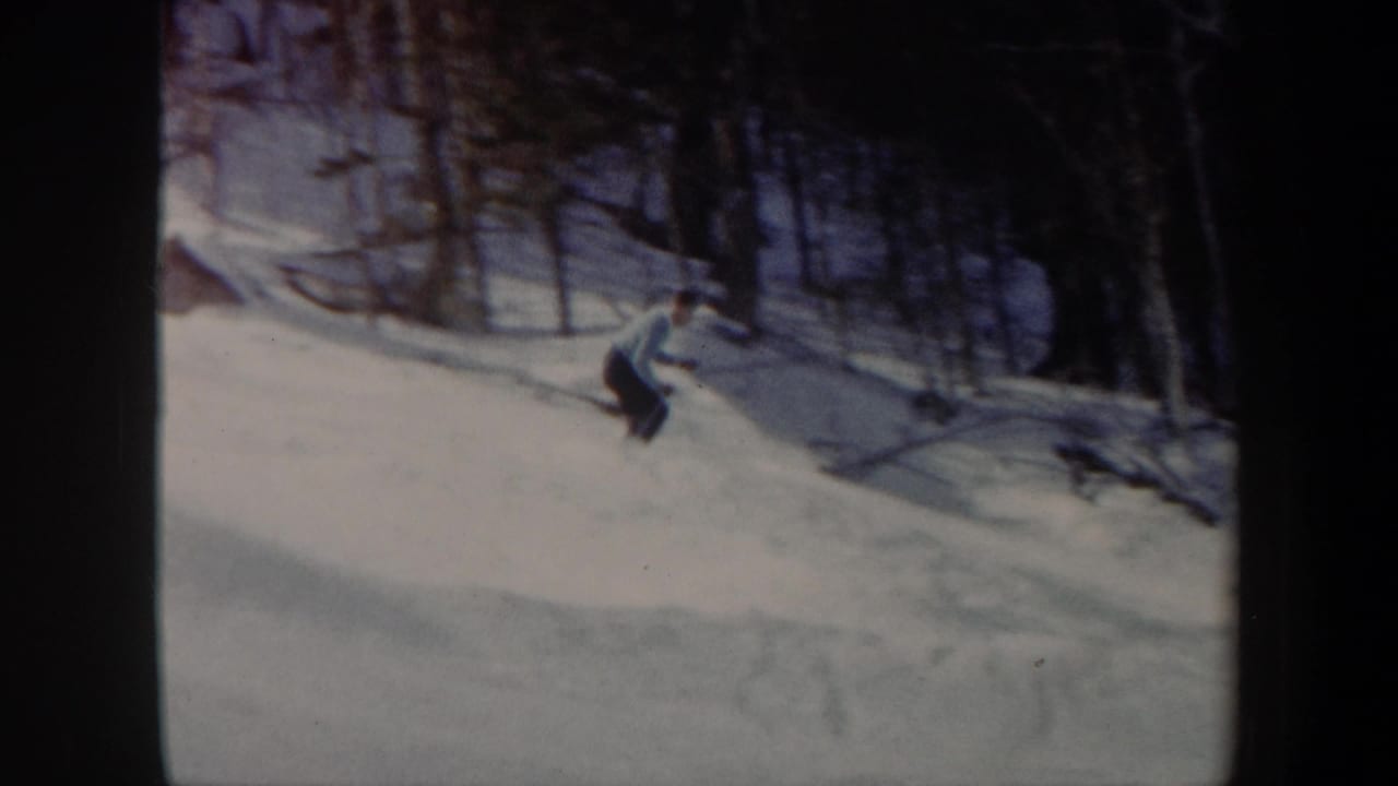 Adult man skis across a snowy Vermont hillside in 1962 8mm home-movie footage, with bare trees and dark woods behind him.