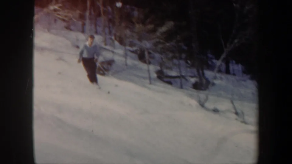 An adult skier in a light top and dark pants moves toward the camera on a snowy Vermont hillside in home-movie footage.