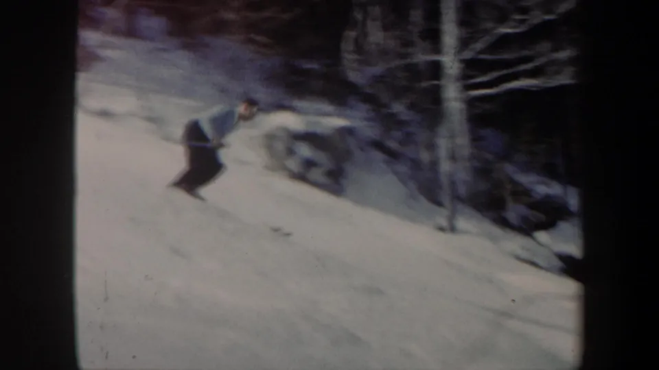 The skier leans into the descent on a snowy wooded slope, with 8mm softness and winter trees visible around him.